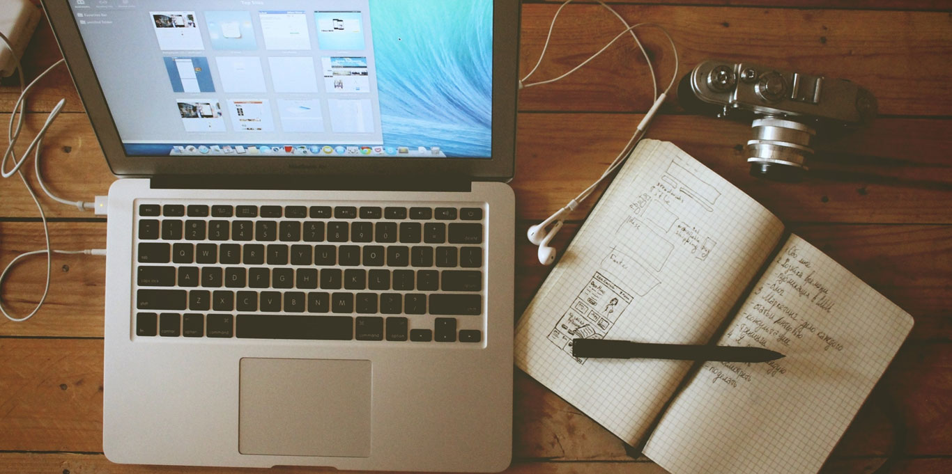 Camera, laptop, headphones and notebook open on a wooden desk